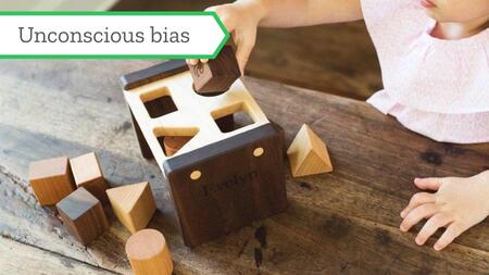 A child holding a square wooden block tries to put it into a wooden shape sorter.